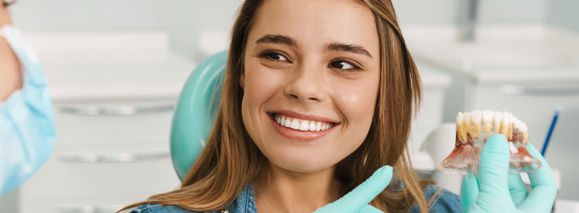 A woman is smiling while seated in a dental chair, with her mouth open to receive dental treatment.