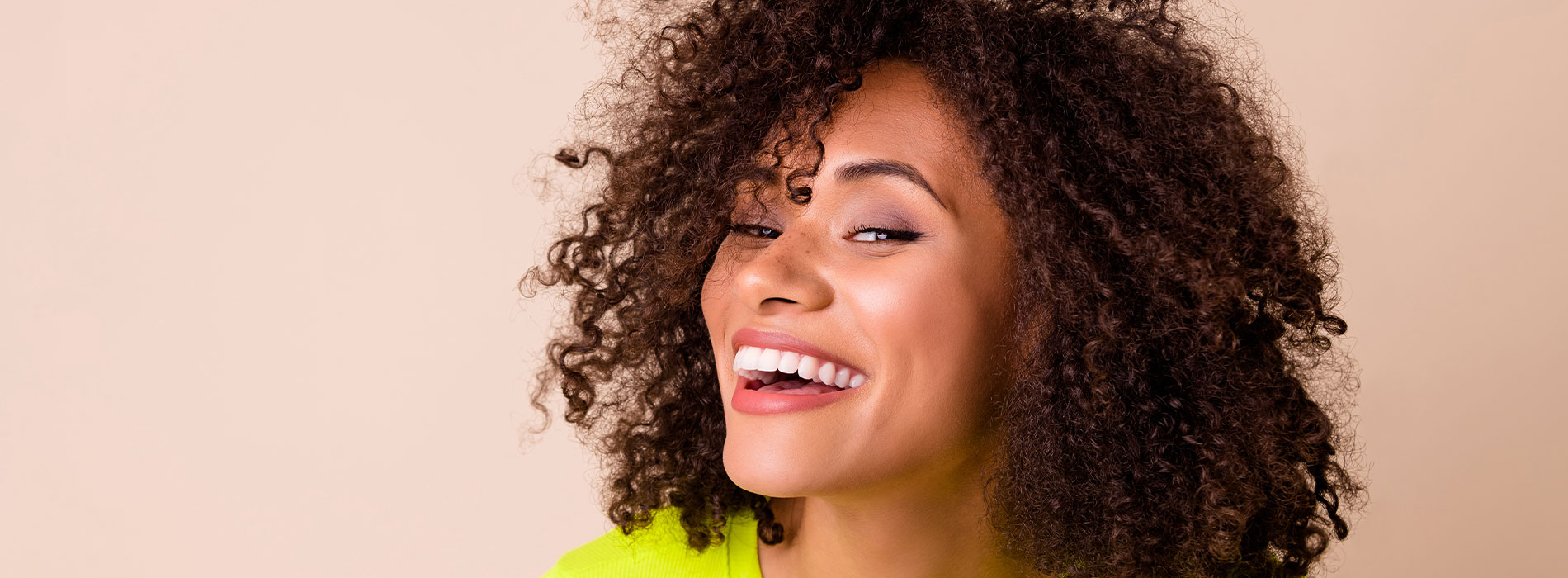 The image shows a person with curly hair, smiling, against a light background.