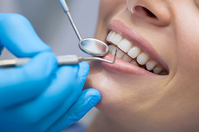 The image shows a person receiving dental care, with a focus on a dentist performing a procedure while the patient is seated and wearing protective gloves.