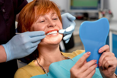 A woman in a dental chair receiving a teeth cleaning, with a dental hygienist wearing gloves and holding tools.